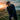 Man in a dark jacket standing on a grassy hill with a sunset or sunrise in the background.