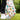 Colorful golf glove with fruit patterns and a matching golf ball on a tee, set against a blurred green outdoor background.