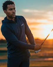 Man holding a golf club with a sunset in the background