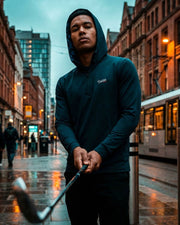 Person holding a golf club on a city street with a train in the background