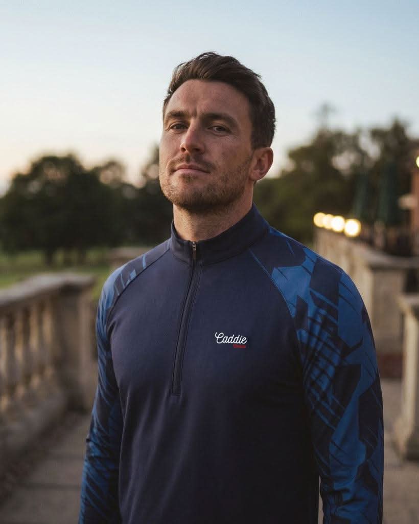 Man wearing a blue and black sports jacket with 'Caddie' branding outdoors.