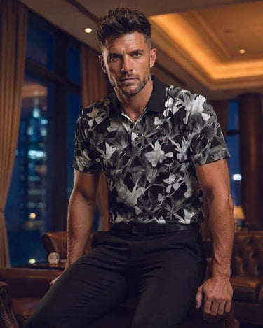 Man wearing a black and gray floral shirt sitting in an elegant room with city lights in the background