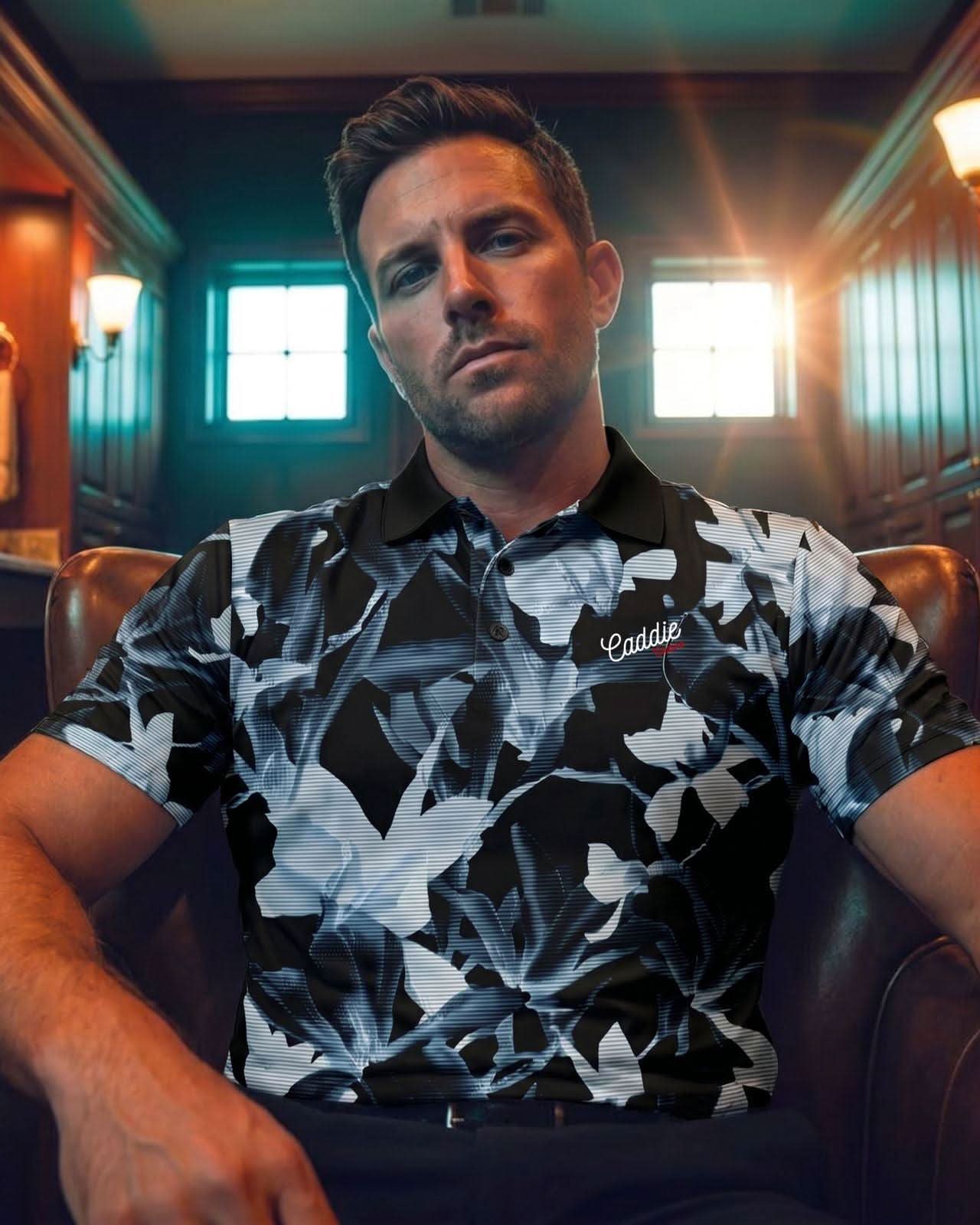 Man wearing a black and white floral patterned shirt sitting in a room with wooden walls and lights.