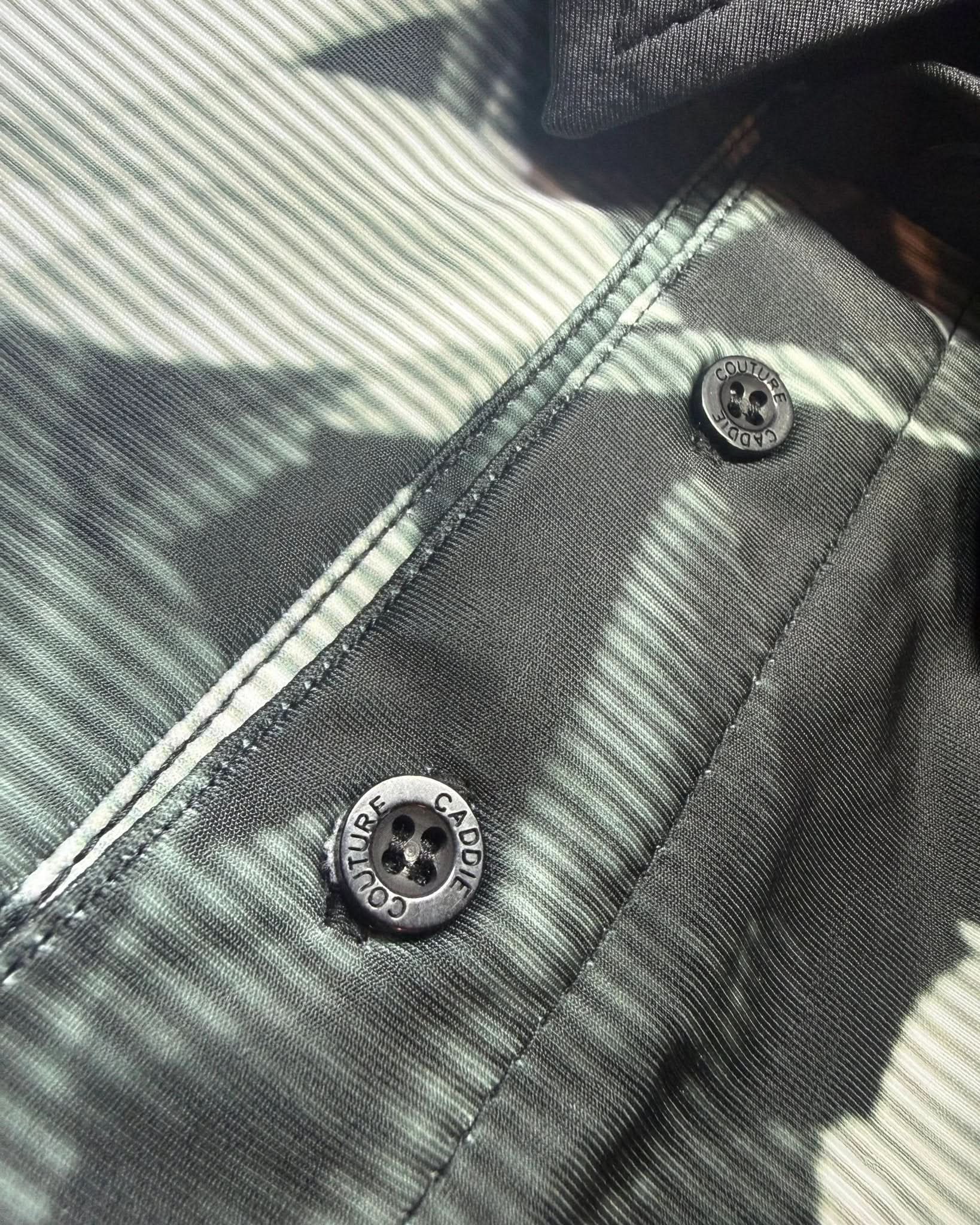 Close-up of a grey shirt with buttons and 'Caddie Couture' branding.