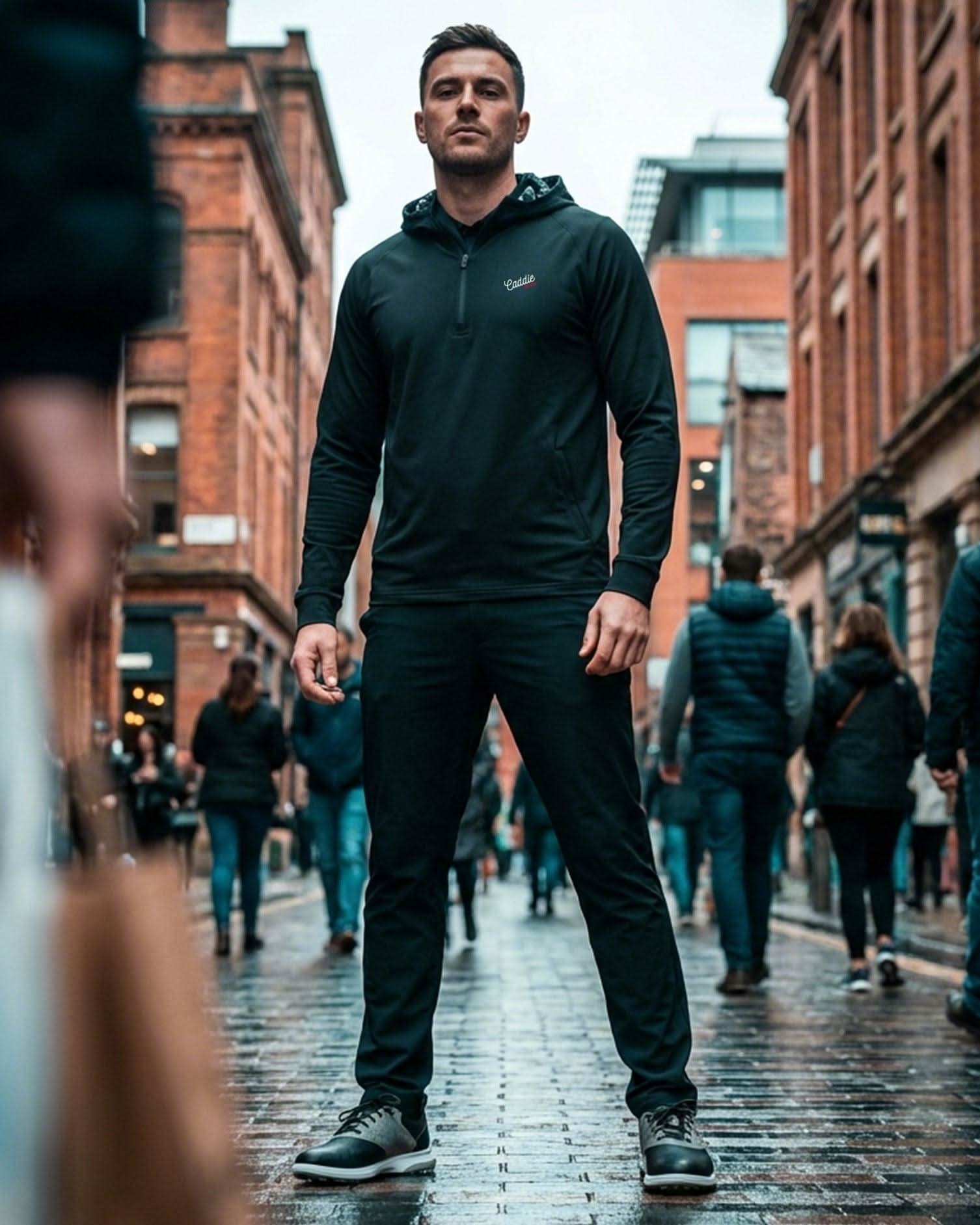 Man in a dark outfit walking down a busy street with brick buildings.