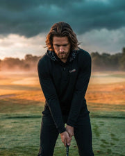 Man playing golf on a grassy field with a dramatic sky