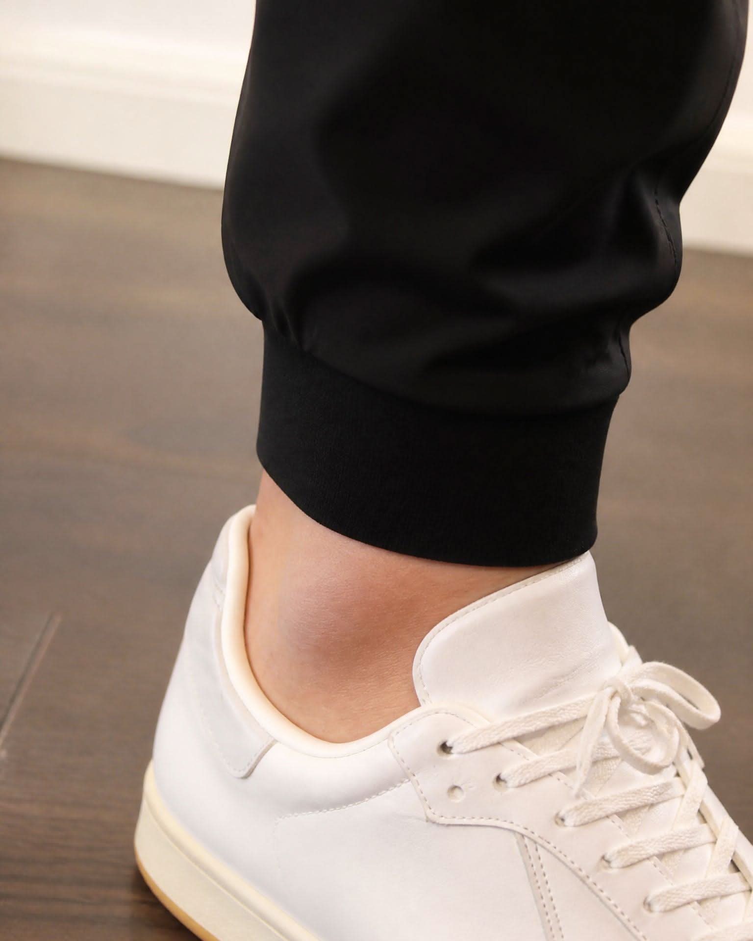 Person wearing black pants and white sneakers on a wooden floor