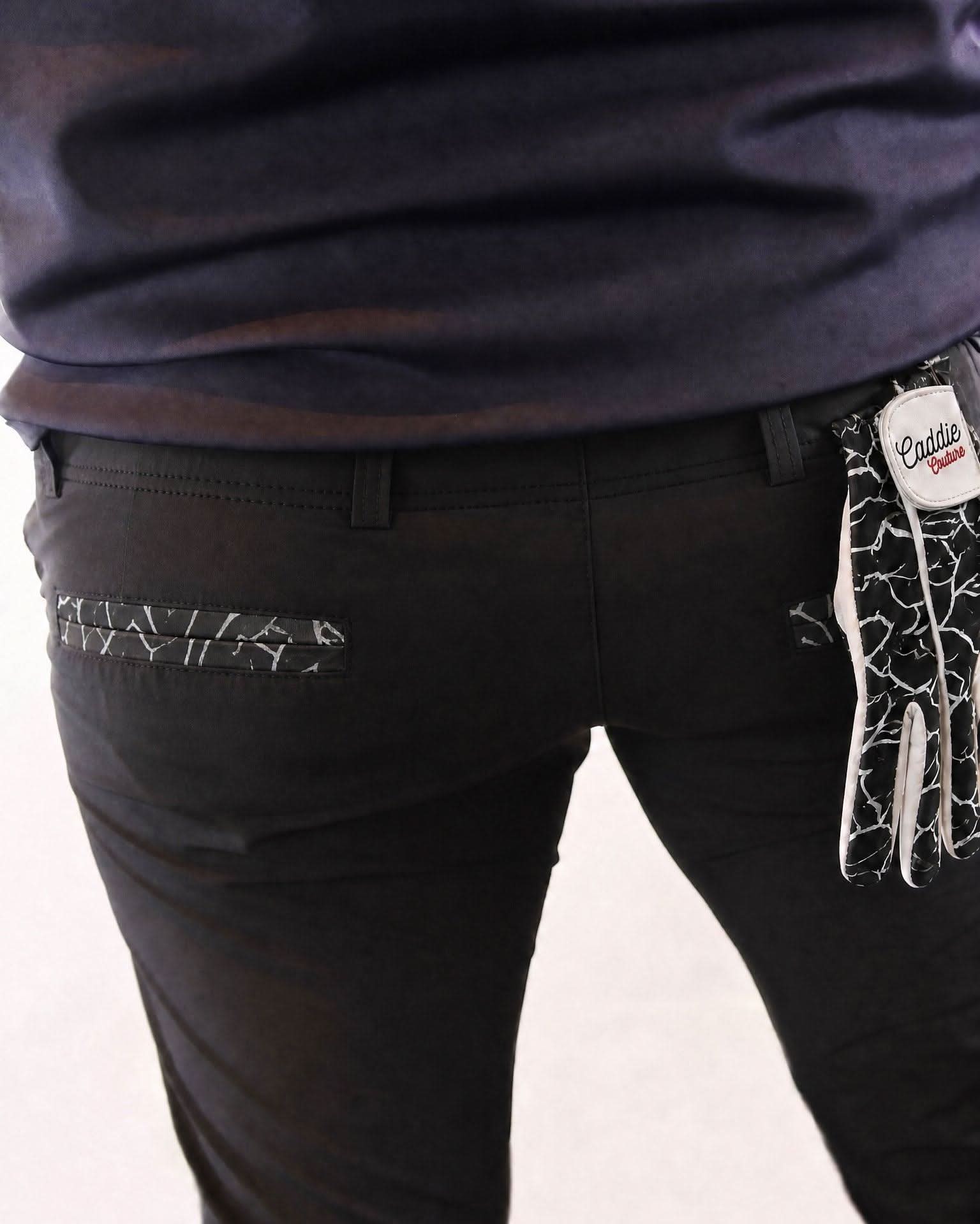 Black pants with decorative stitching and a visible brand tag on a plain background