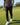 Person wearing a black and white patterned shirt, black pants, and white shoes on a golf course.