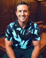Man wearing a blue and black patterned shirt sitting in a wooden locker room.