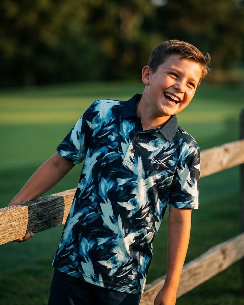 Young boy in a patterned shirt standing by a wooden fence with a blurred green background