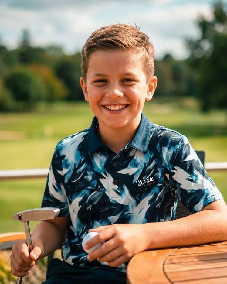Young boy holding a golf club and smiling outdoors on a golf course