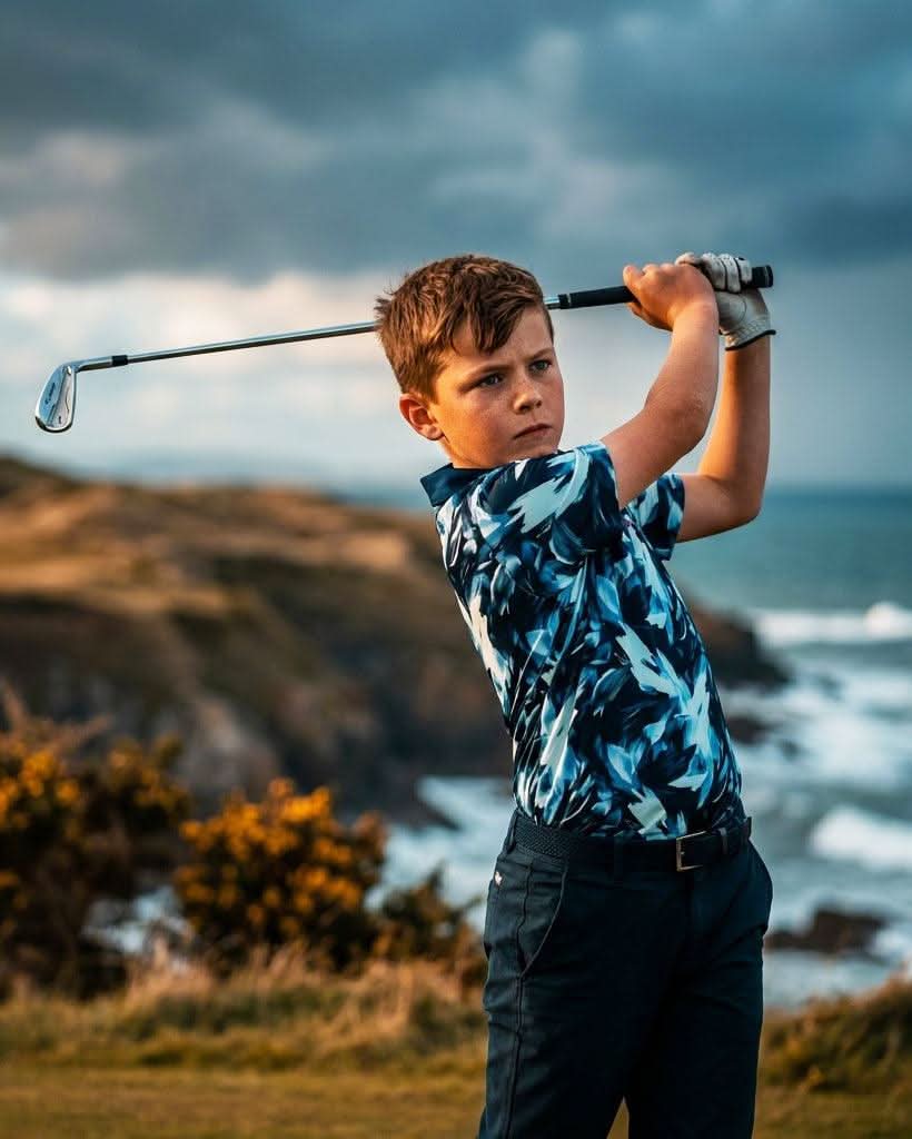 Young boy playing golf on a coastal cliff with ocean and sky in the background