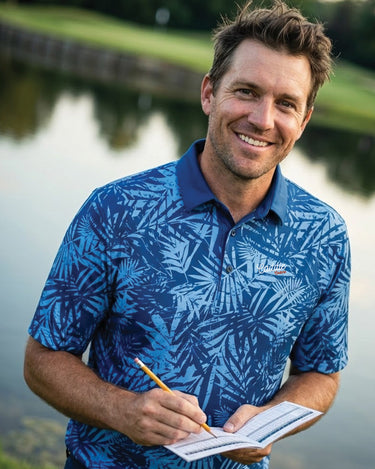 Man in a blue patterned shirt holding a pencil and paper by a body of water.
