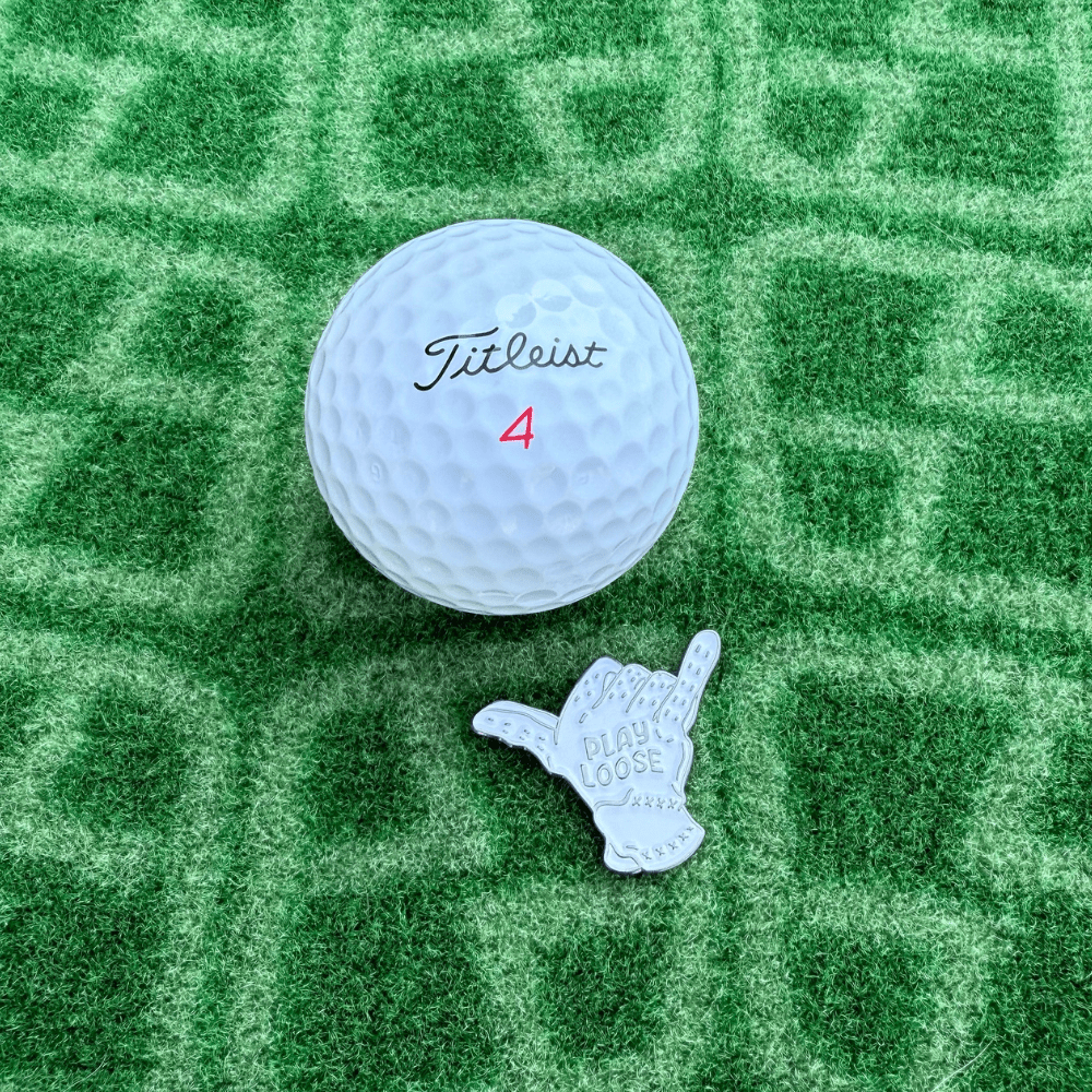 Titleist golf ball with a glove shaped golf ball marker on a green textured surface