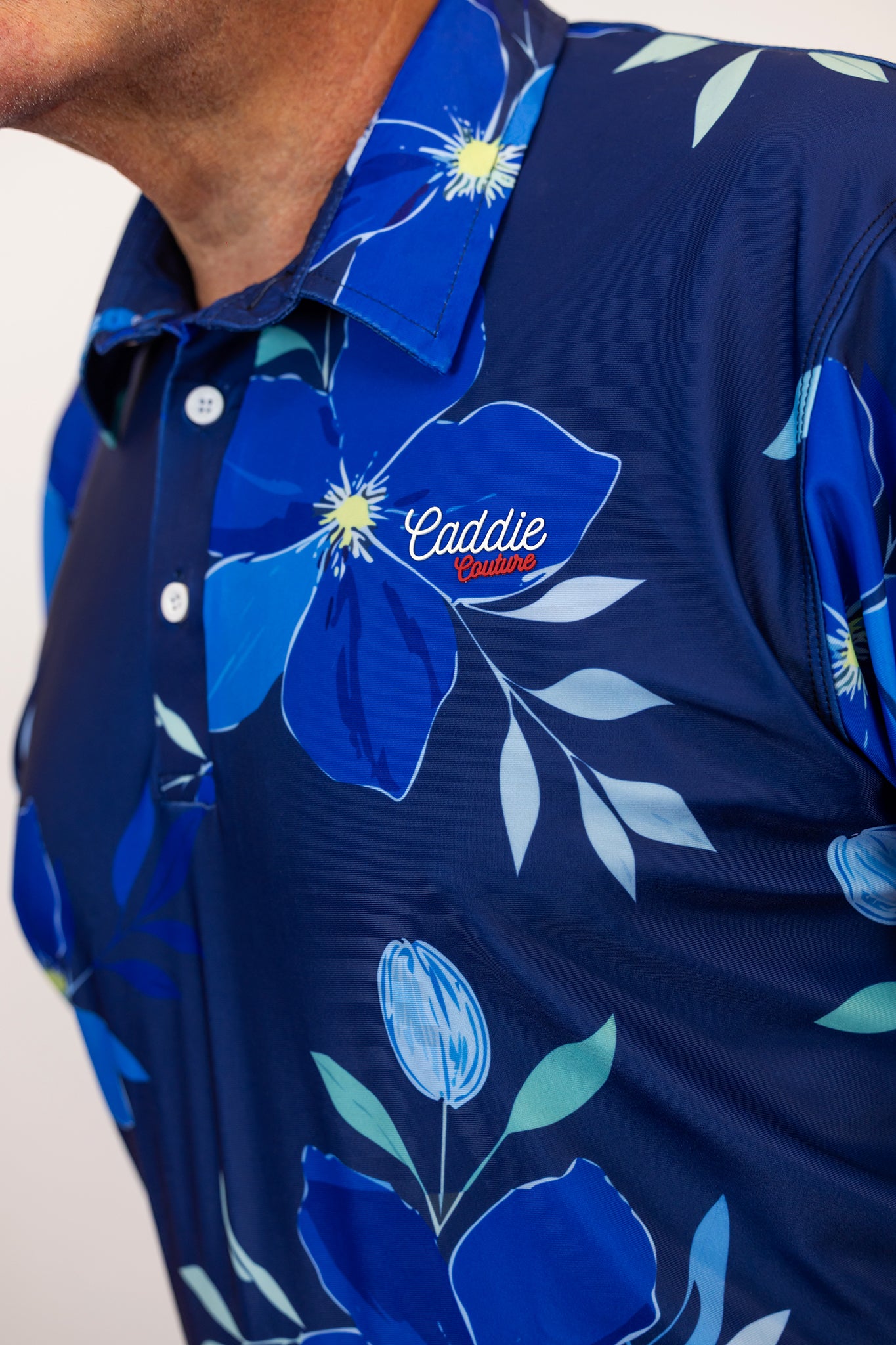Navy blue golf shirt with floral design and 'Caddie Couture' logo on a white background