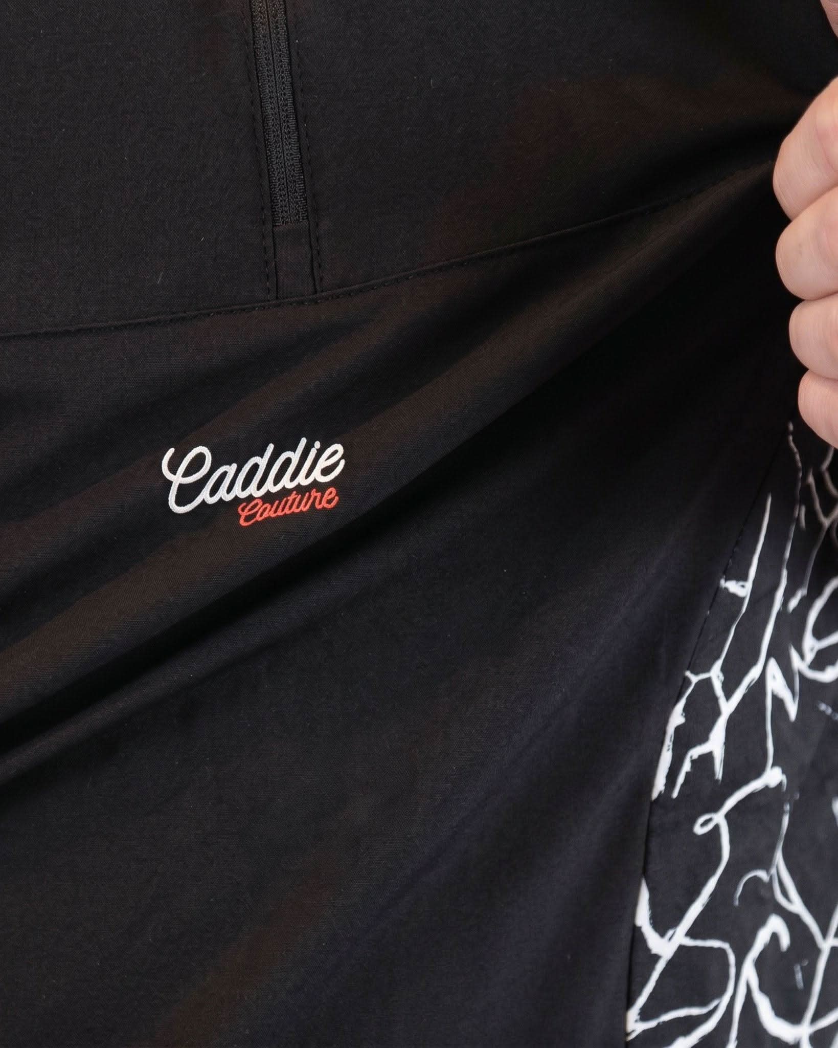 Black jacket with 'Caddie' logo and white design on sleeve, held by a hand.