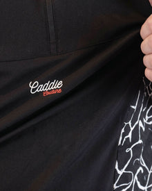 Black jacket with 'Caddie' logo and white design on sleeve, held by a hand.