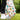 Colorful golf glove with fruit patterns and a matching golf ball on a tee, set against a blurred green outdoor background.