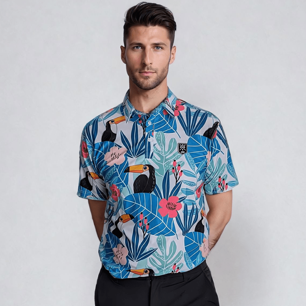 A man wearing a short-sleeved tropical print golf polo shirt with various colors, including blue, green, and pink, featuring a bird species, palm trees, and other foliage.