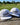 Two white caps with 'Caddie Couture' text on a wooden surface with a golf course background.