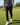 Person wearing a black and white patterned shirt, black pants, and white shoes on a golf course.
