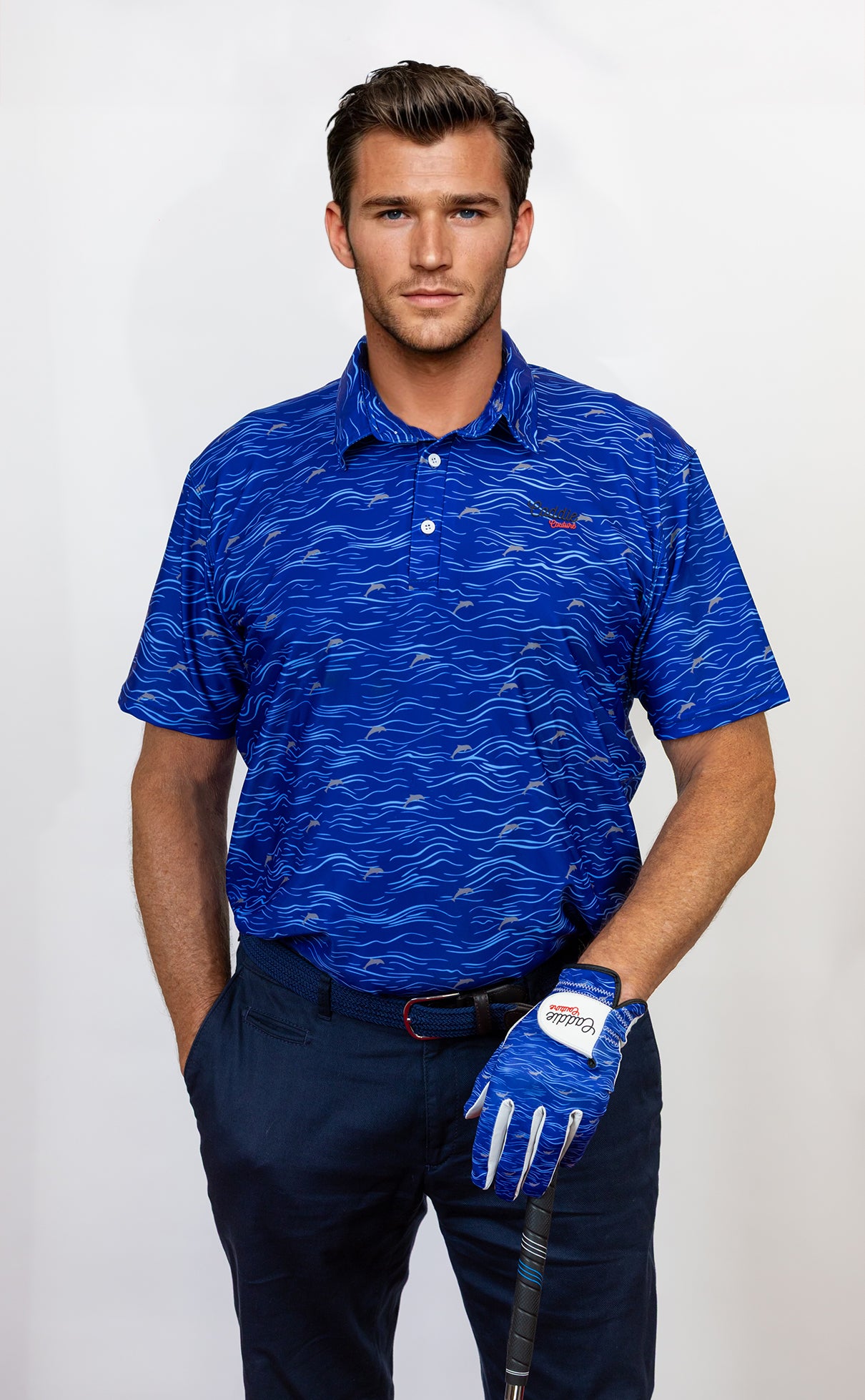 Man wearing a blue patterned golf polo shirt and navy pants, holding a golf club on a white background